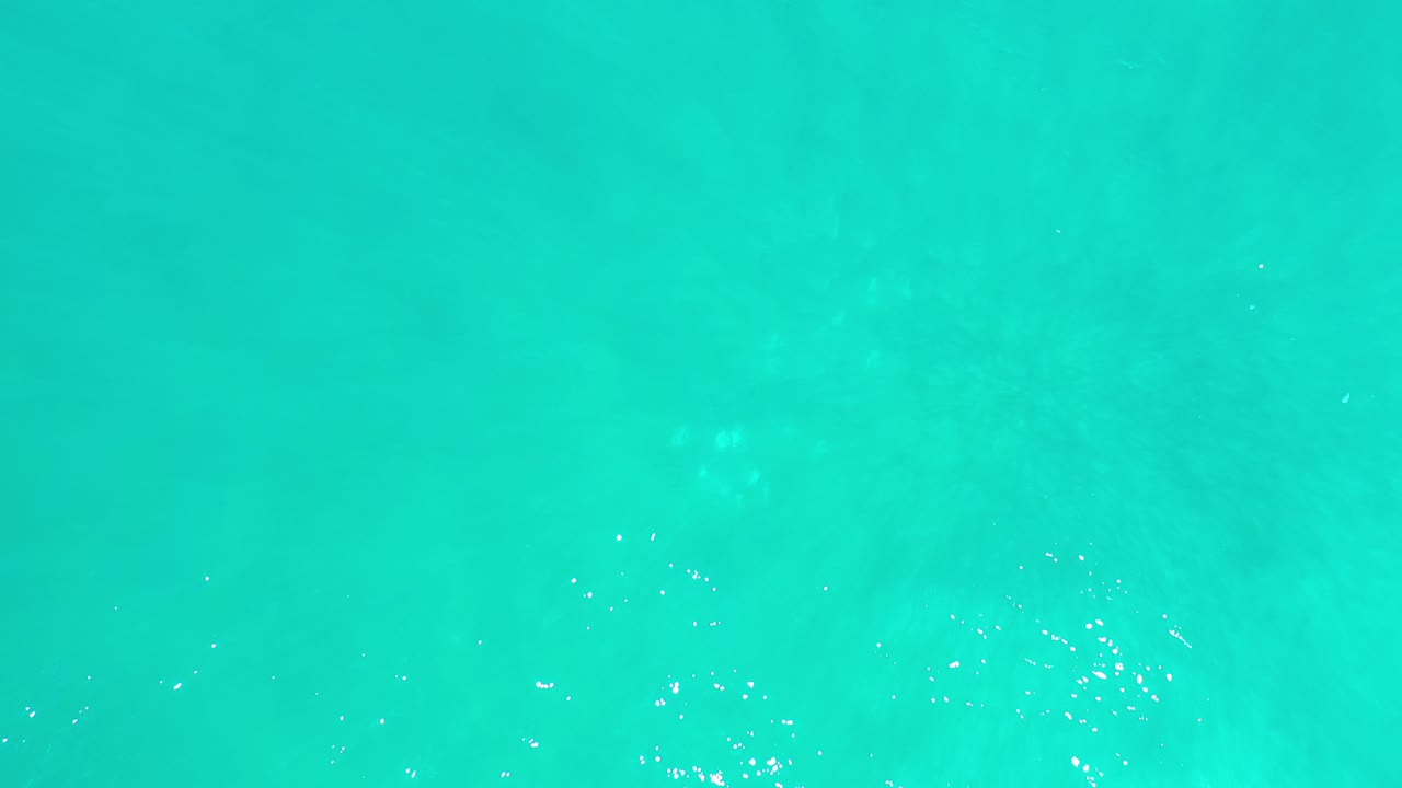 Top-down view of turquoise green ocean water in Los Cabos, Mexico, with scattered white highlights near the surface and no visible people.