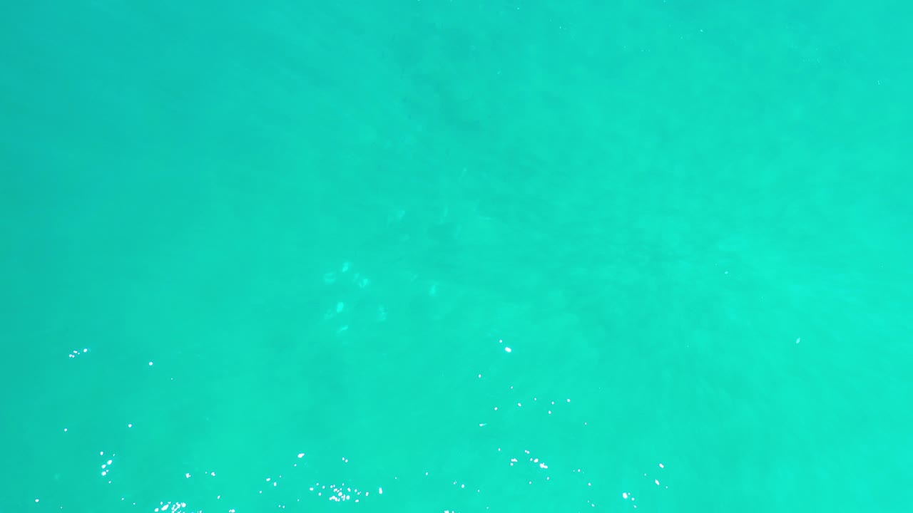 Overhead view of turquoise ocean water in Los Cabos, Mexico, with faint darker patches below the surface and no visible people.
