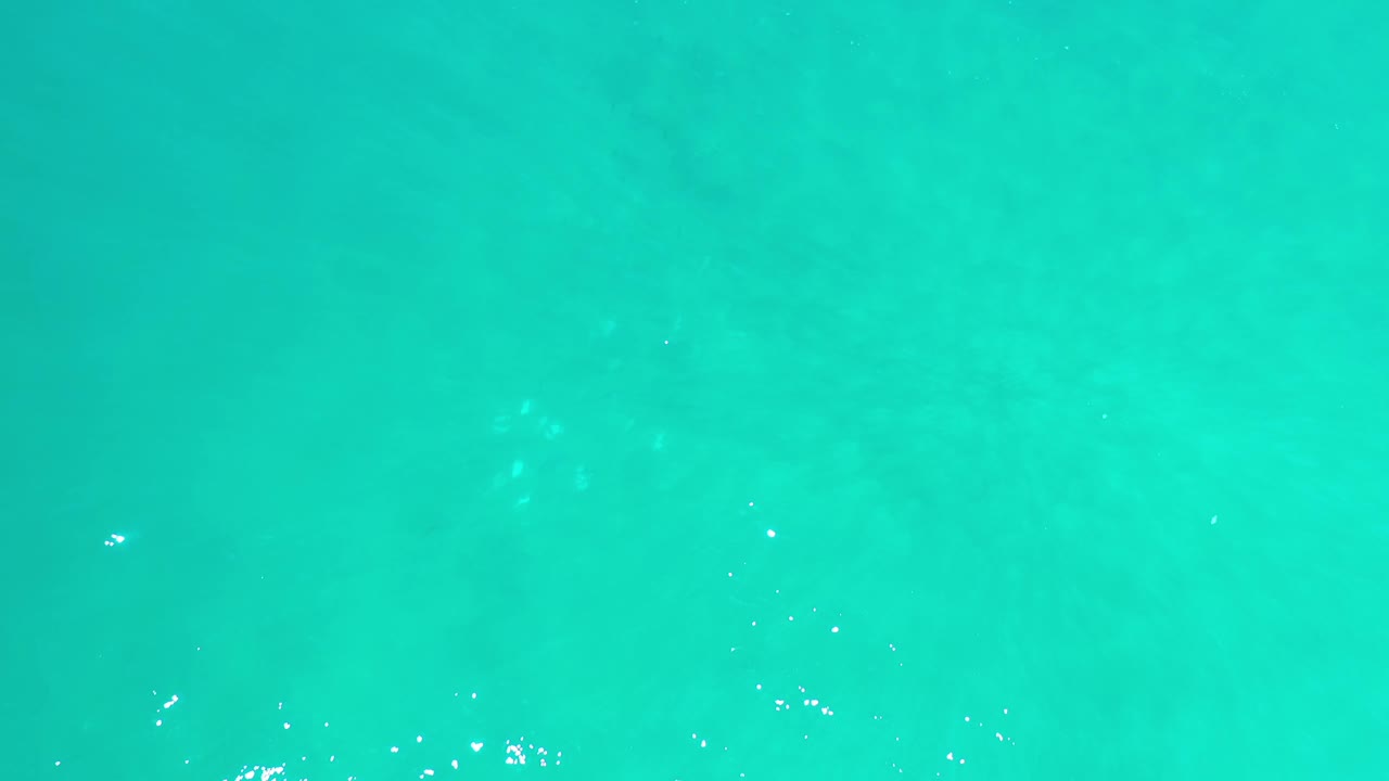 Emerald-blue ocean surface in Los Cabos, Mexico, shown from above with scattered white glints near the lower part of the frame and no visible people.