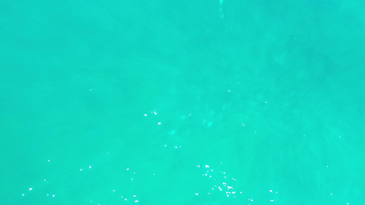 Aqua ocean water fills the image in Los Cabos, Mexico, with small bright reflection specks shifting across the surface and no visible people.