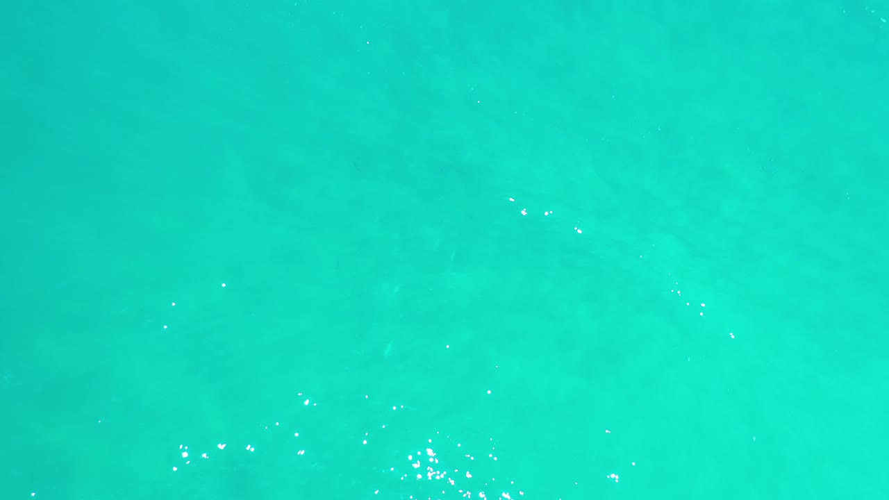 Clear green ocean surface fills the frame in Los Cabos, Mexico, with a soft diagonal texture under the water and no visible people.