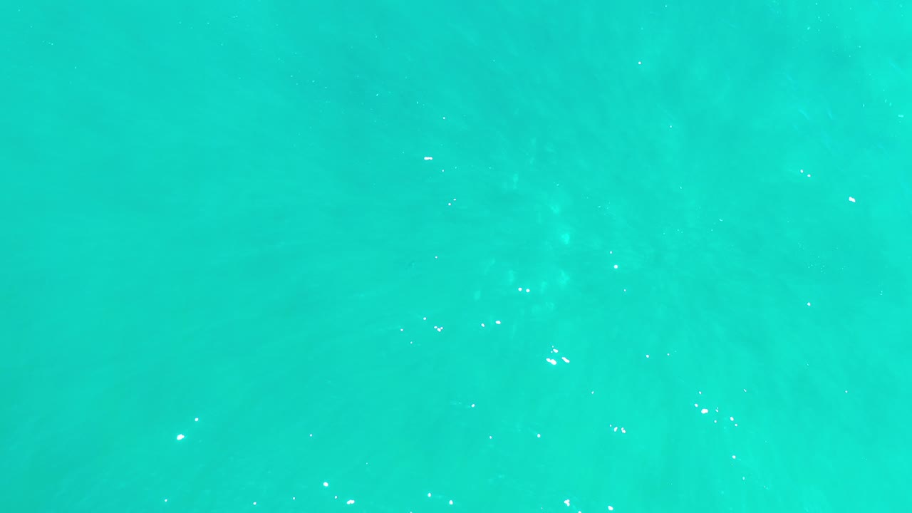 Top-down view of turquoise water in Los Cabos, Mexico, with faint darker patches below the surface and no visible people.