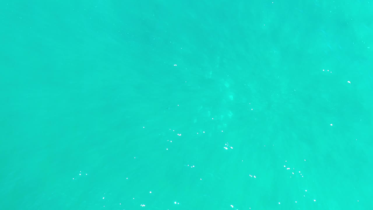 Aqua water fills the frame in Los Cabos, Mexico, with scattered white sparkles near the surface and no visible people.