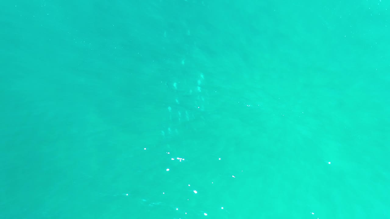 Opening frame of turquoise ocean water in Los Cabos, Mexico, with faint sandy bottom texture under small ripples and no visible people.