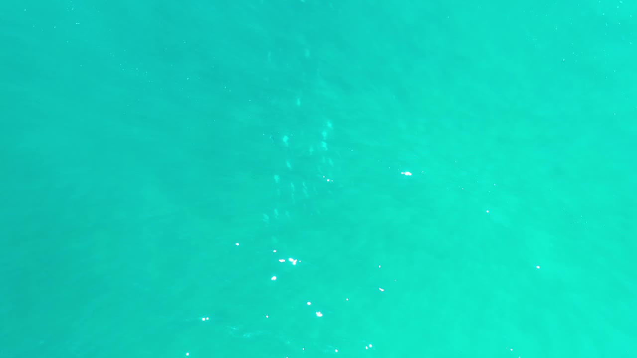 Blue-green ocean water in Los Cabos, Mexico, fills the frame as subtle wave patterns reveal a pale sandy bottom below, with no visible people.