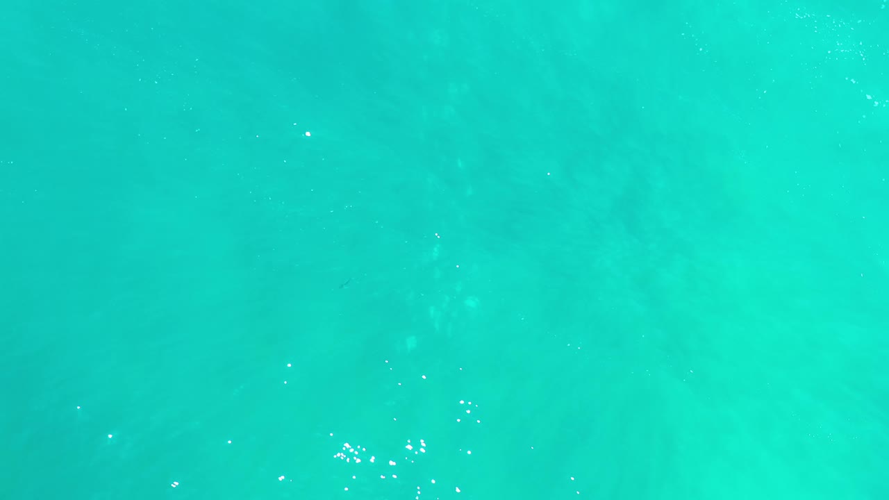 Clear blue Los Cabos water shows a loose cluster of bright reflections near the lower left, with no shoreline, vessels, or visible people.