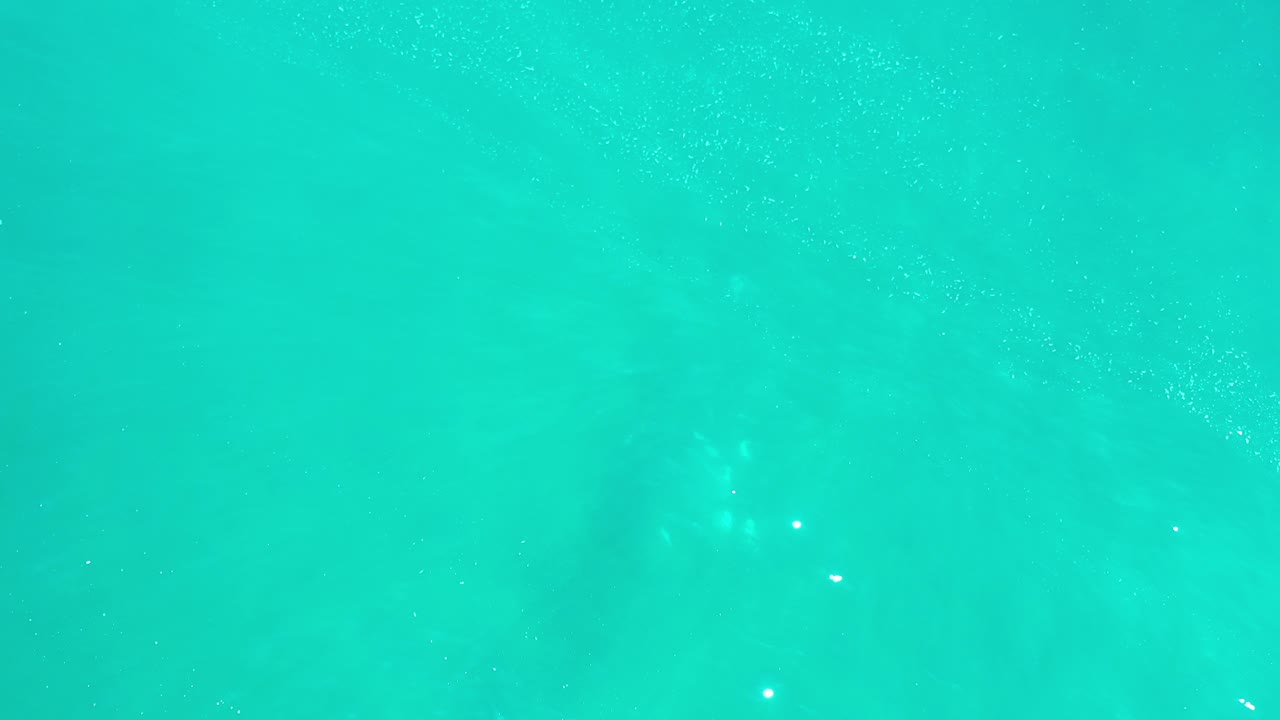 Turquoise Los Cabos seawater fills the frame with faint pale patches below the surface and no visible people.