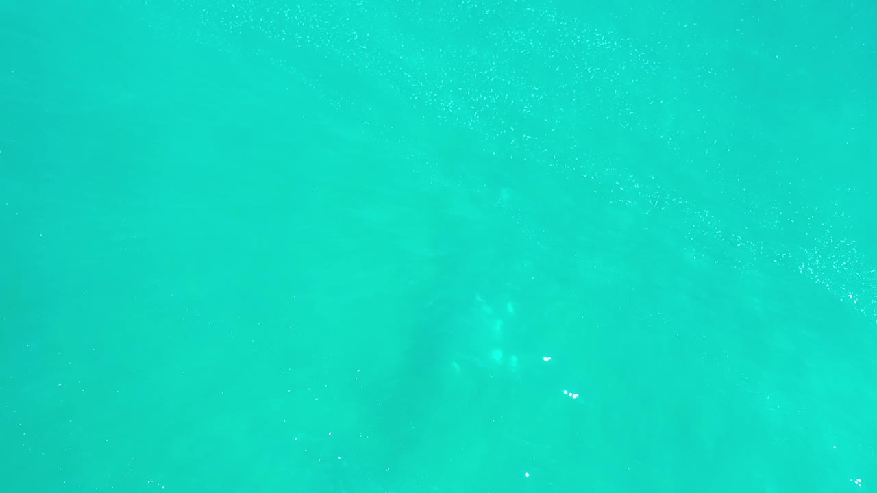 Green-blue Los Cabos water shows soft cloudy shapes under the surface, scattered specks, and no visible people.