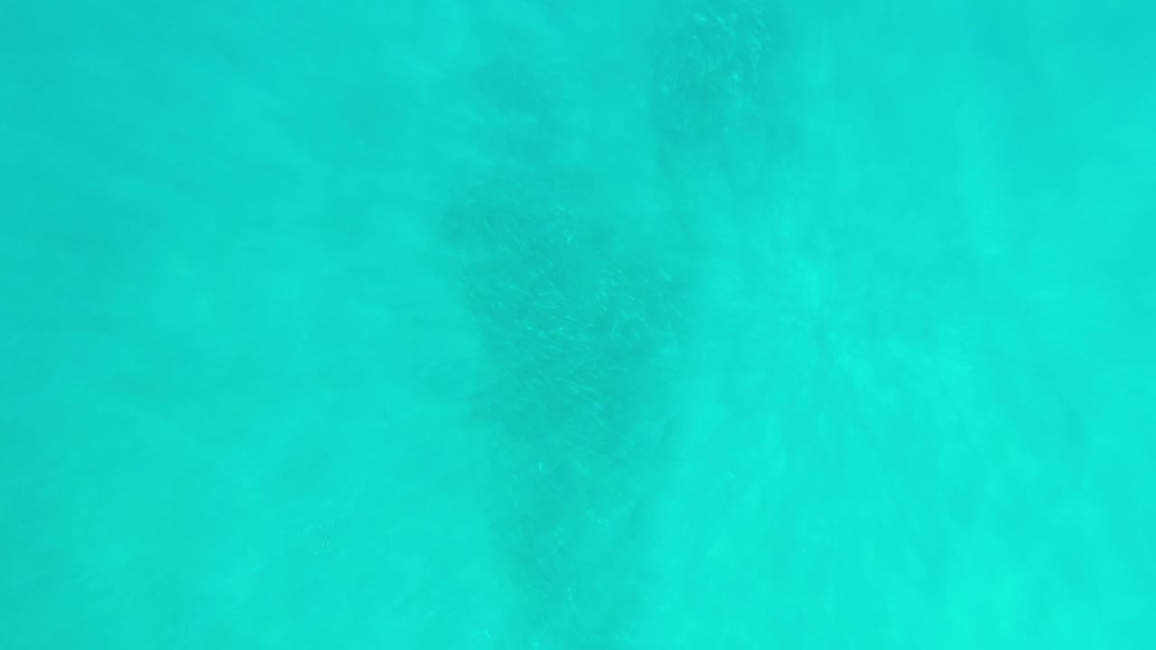 Overhead view of turquoise ocean water in Los Cabos, Mexico, with faint darker patches below the surface and no visible people.