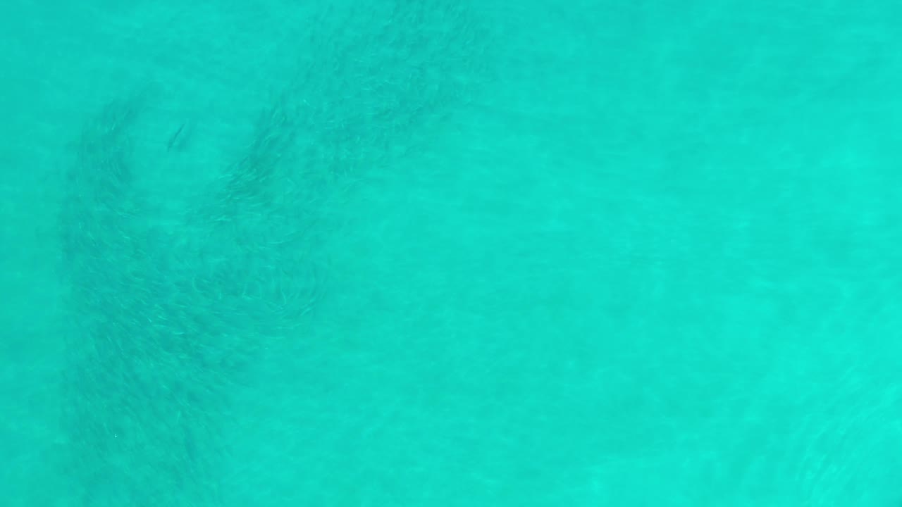 Clear turquoise Los Cabos water shows darker underwater patches near the upper area, with no visible people.