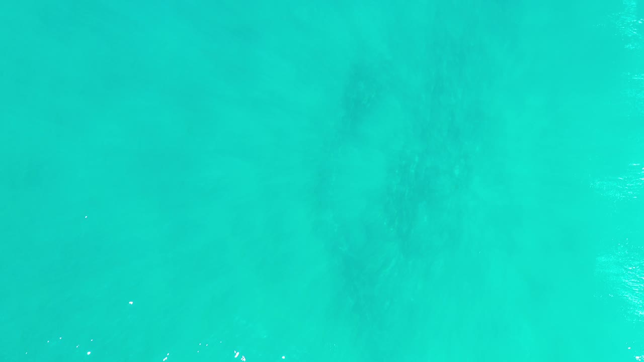 Overhead view of turquoise-green ocean water in Los Cabos, Mexico, with faint darker areas below the surface and no visible people.