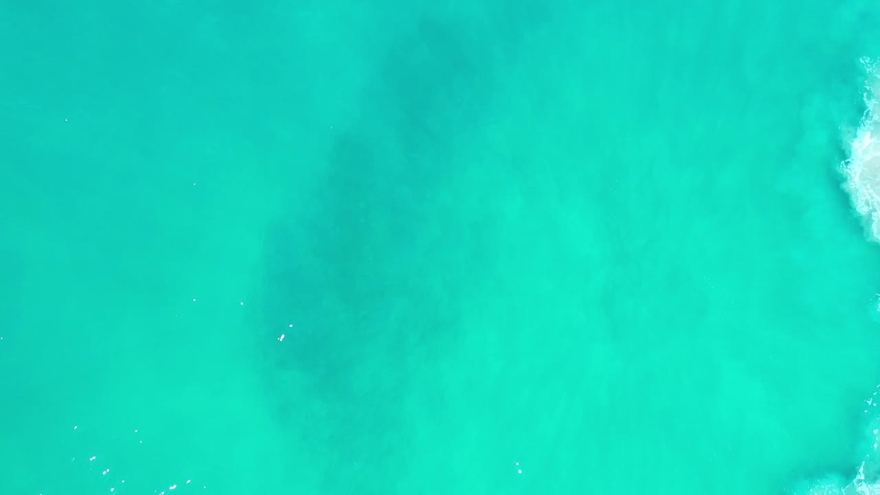 Bright turquoise water with a darker underwater area and small flecks of white foam.