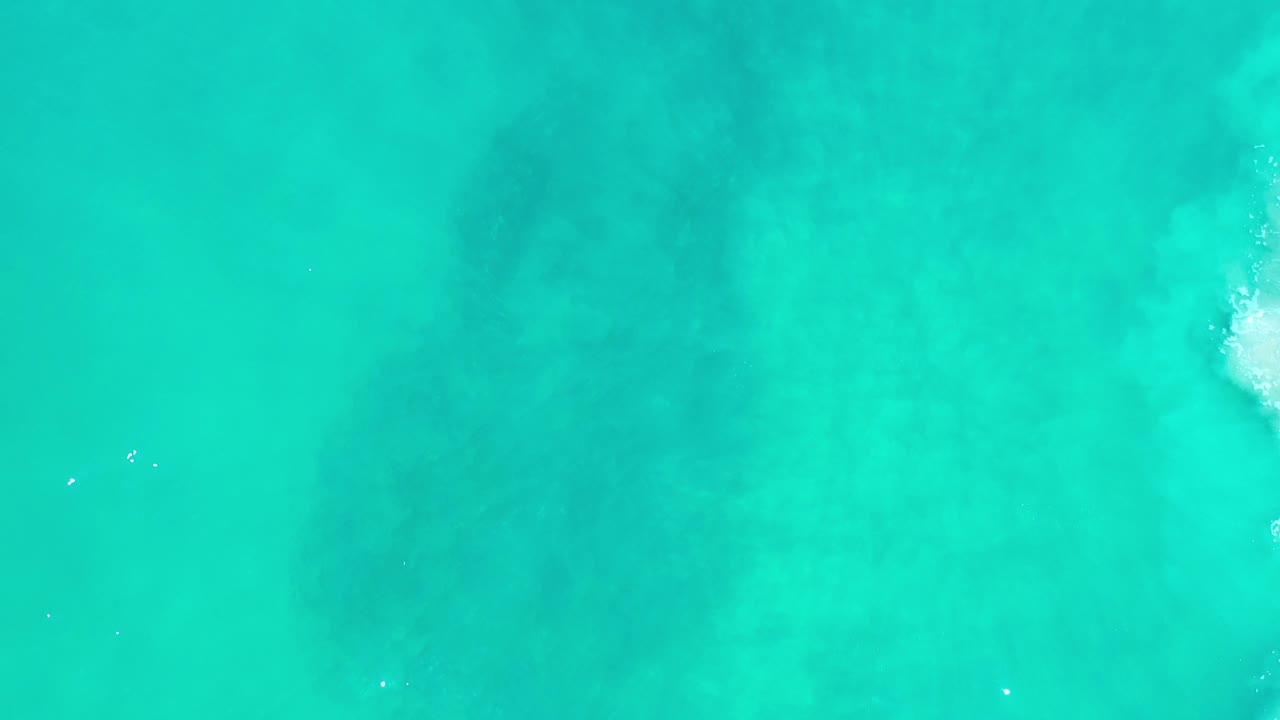 Overhead view of turquoise ocean water in Los Cabos, Mexico, with faint darker patches beneath the surface and no visible people.