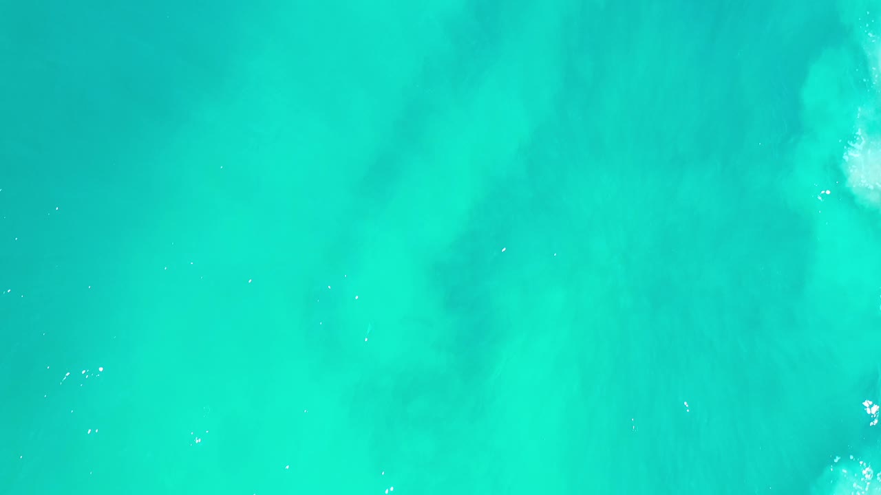 Turquoise seawater with faint foam and sun glints from above.