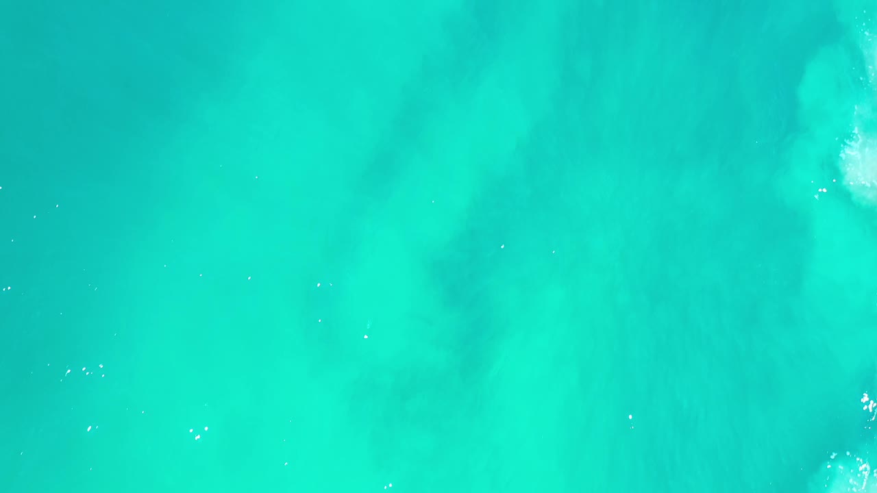 Overhead Los Cabos water frame with clear aqua surface, subtle darker areas under the water, scattered highlights, and no visible people.