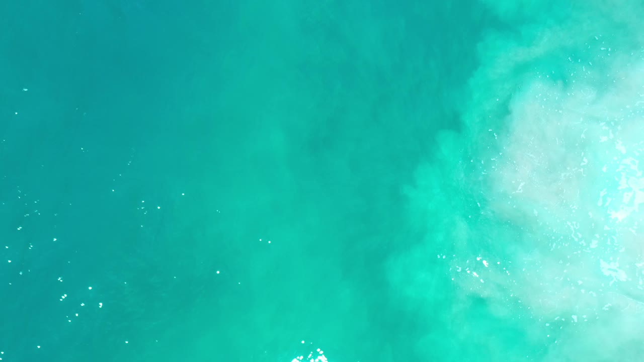 Cyan sea with bright foam patch at the upper right and small sparkle highlights.