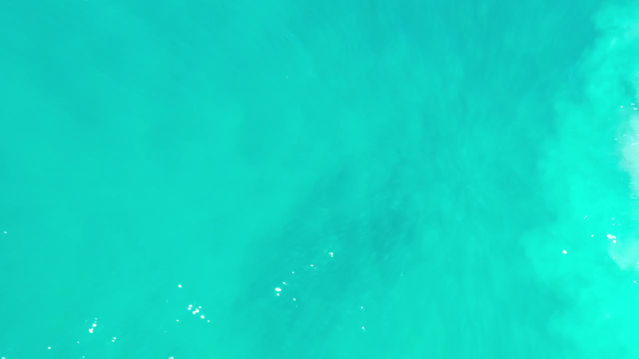 Top-down aerial view of turquoise ocean in Los Cabos, Mexico, with faint pale surf texture near the upper right and no visible people.