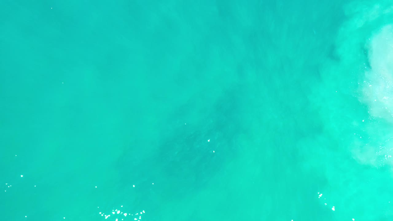 Turquoise sea with a brighter vertical patch of wave foam near the top.
