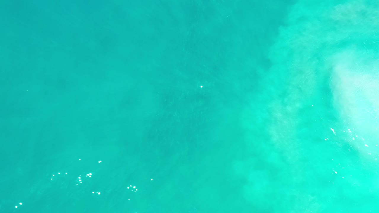 Overhead view of blue green ocean water in Los Cabos, Mexico, with a pale foam patch near the upper right and no visible people.