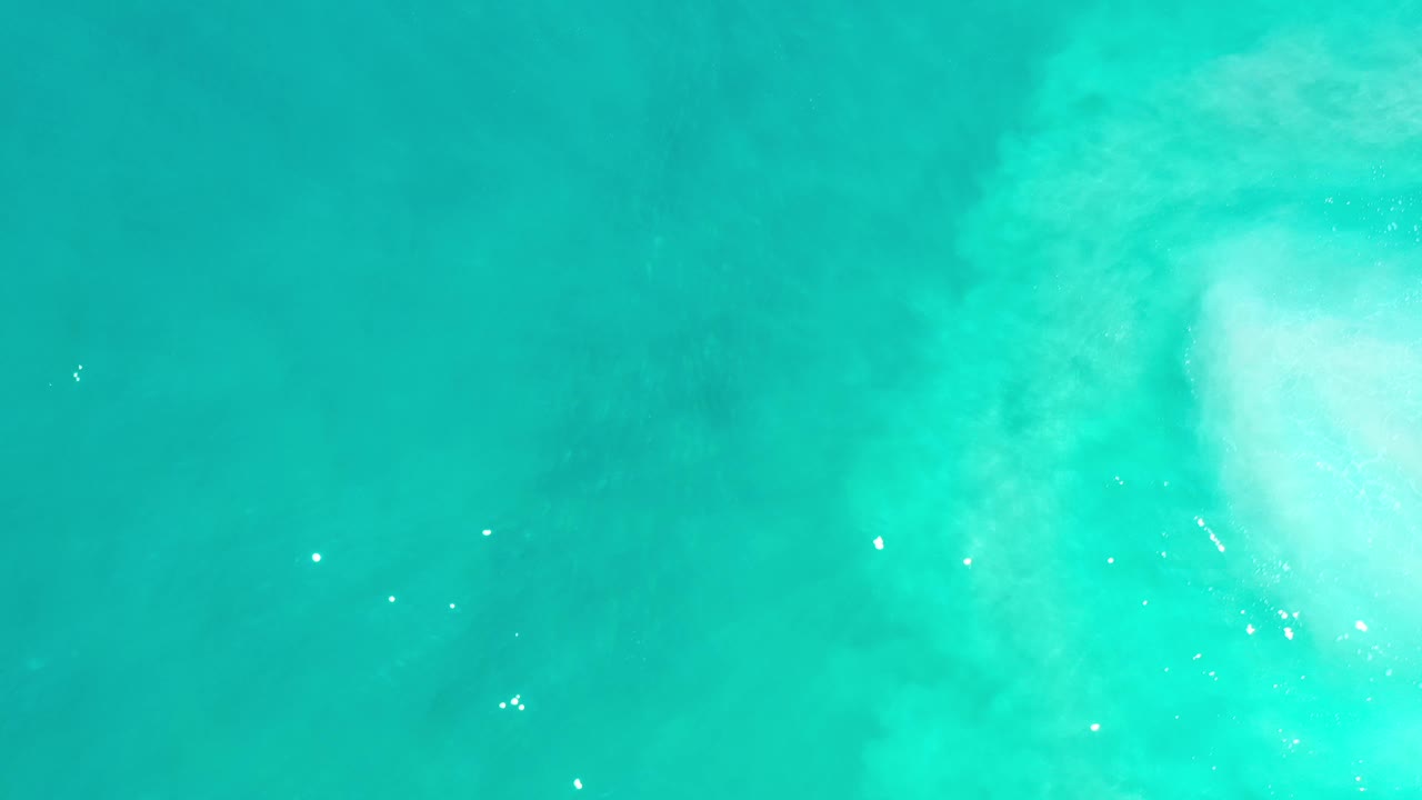 Turquoise sea surface with a white foamy area in the upper right corner.