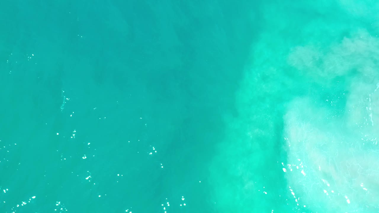 Overhead Los Cabos sea surface with a soft white area drifting through the upper center and no visible people.