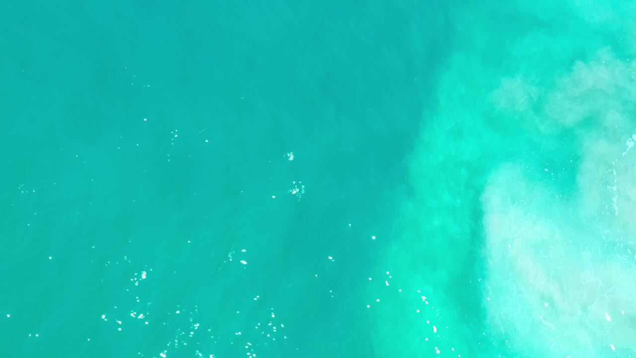 Aerial blue-green water with pale streaking at the right edge.