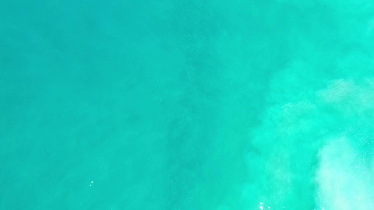 Top-down view of turquoise ocean water in Los Cabos, Mexico with pale cloudy wave wash near the center and no visible people.