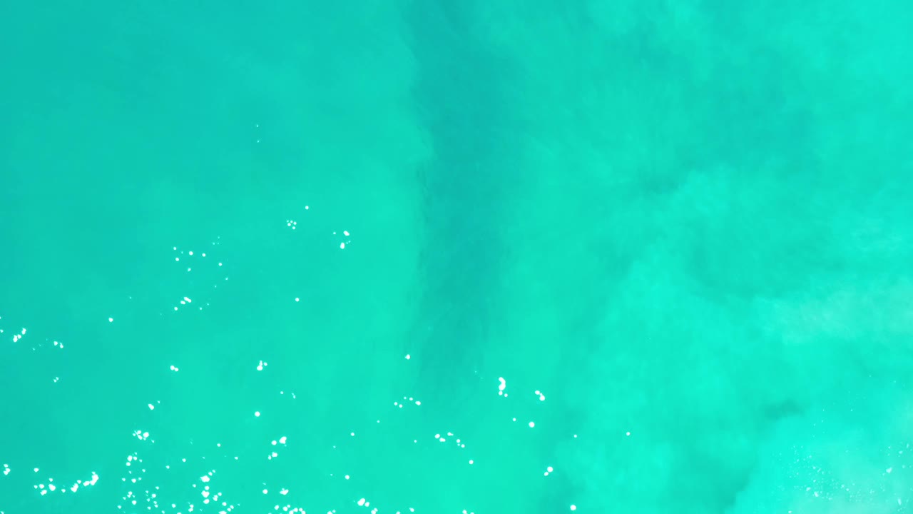 Overhead view of turquoise-green water in Los Cabos, Mexico, with scattered bright sun glints near the lower edge and no visible people.