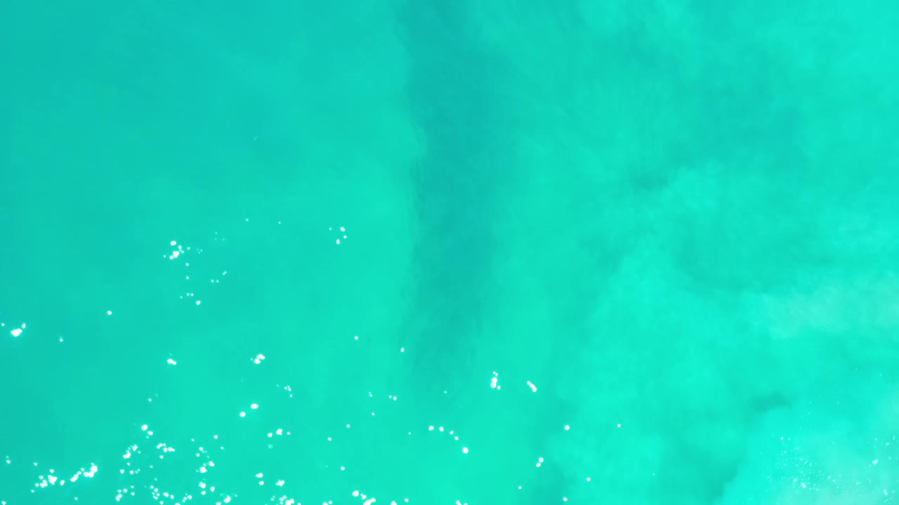 Overhead Los Cabos water frame with pale underwater clouding, soft turquoise color, and small white reflections across the surface with no visible people.