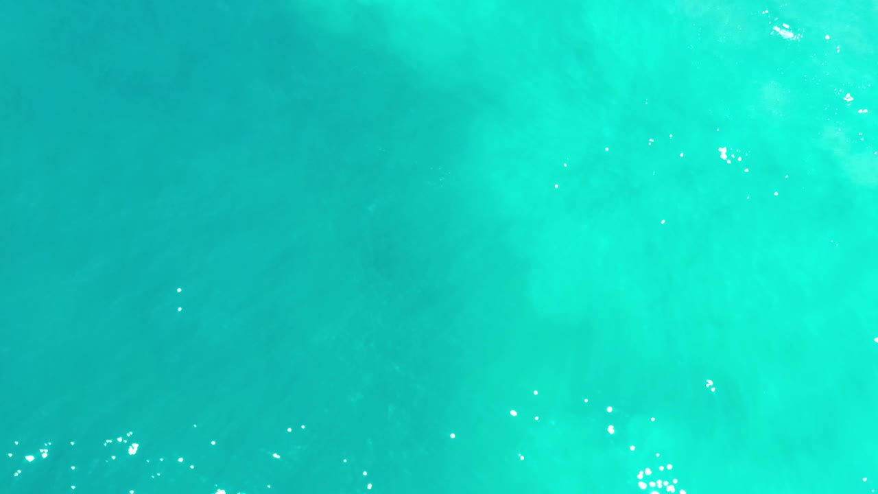 Aqua ocean water fills the frame in Los Cabos, Mexico, with subtle darker patches below the surface and no visible people.