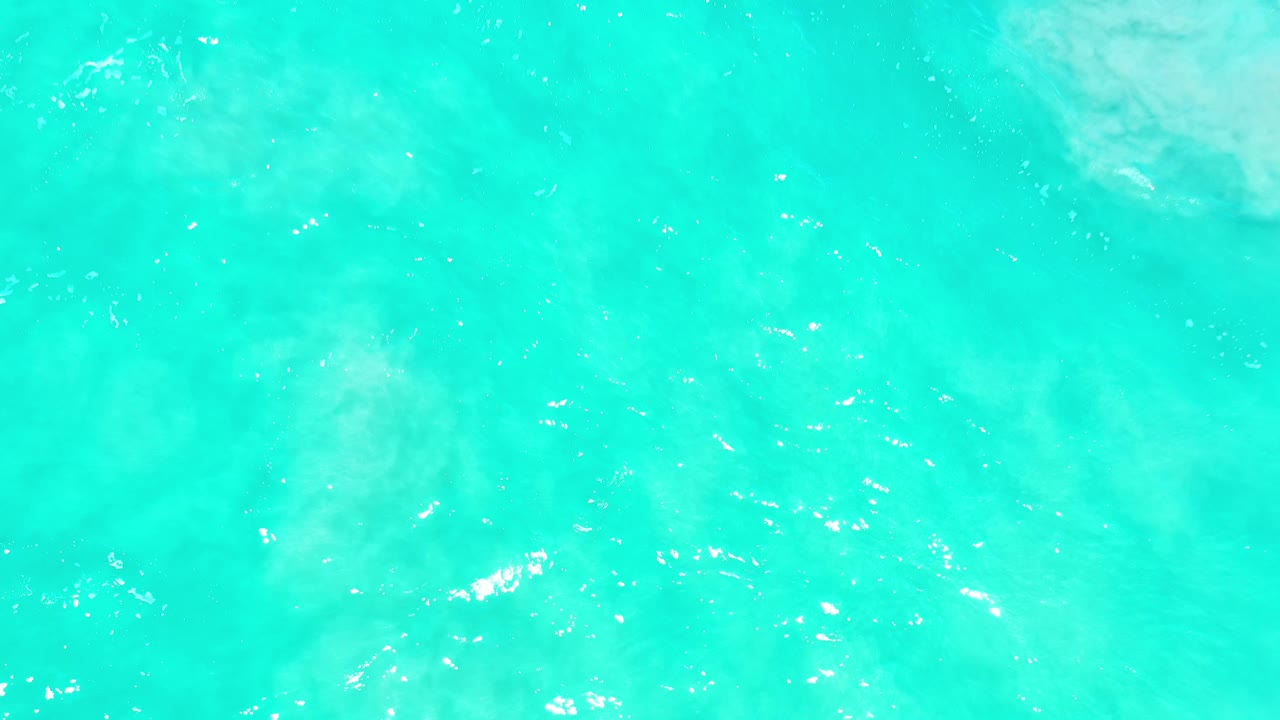 Turquoise ocean water with sun glints and pale surf texture.