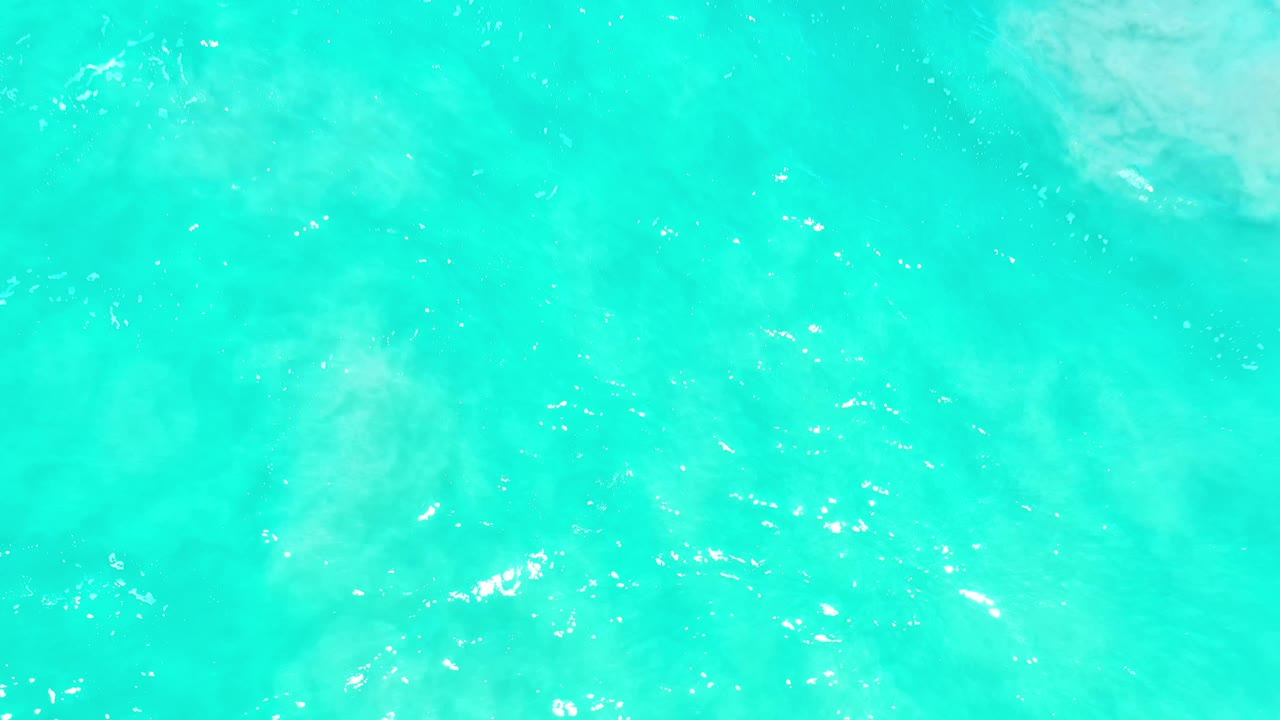 Aqua sea surface in Los Cabos, Mexico, with white foam pushing in from the top of the frame and scattered reflective highlights, no visible people.