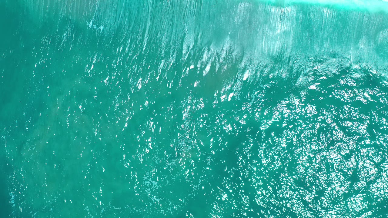 Overhead view of turquoise sea in Los Cabos, Mexico, with a white surf band along the top edge and no visible people.