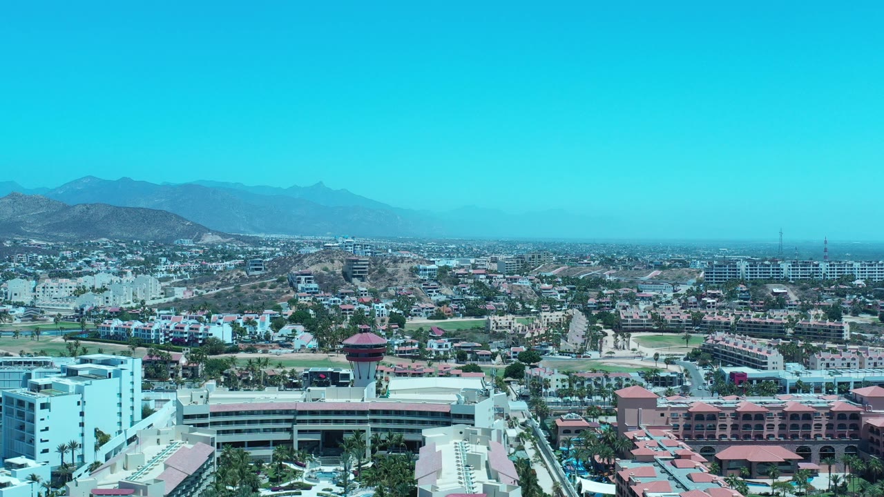 Aerial view of city rooftops with mountains under a bright blue sky.