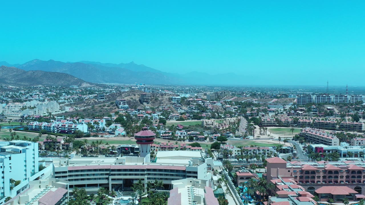 Aerial view of a resort complex, roads, city buildings, mountains, and blue sky.