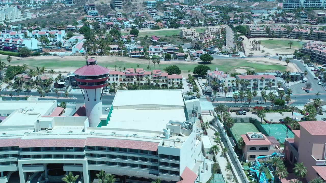 Drone view across a tower, broad flat roof, sports courts, streets, and residential buildings.
