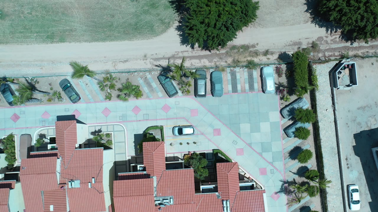 Aerial view of apartment complex edge, parked cars, palm landscaping, and dry field.