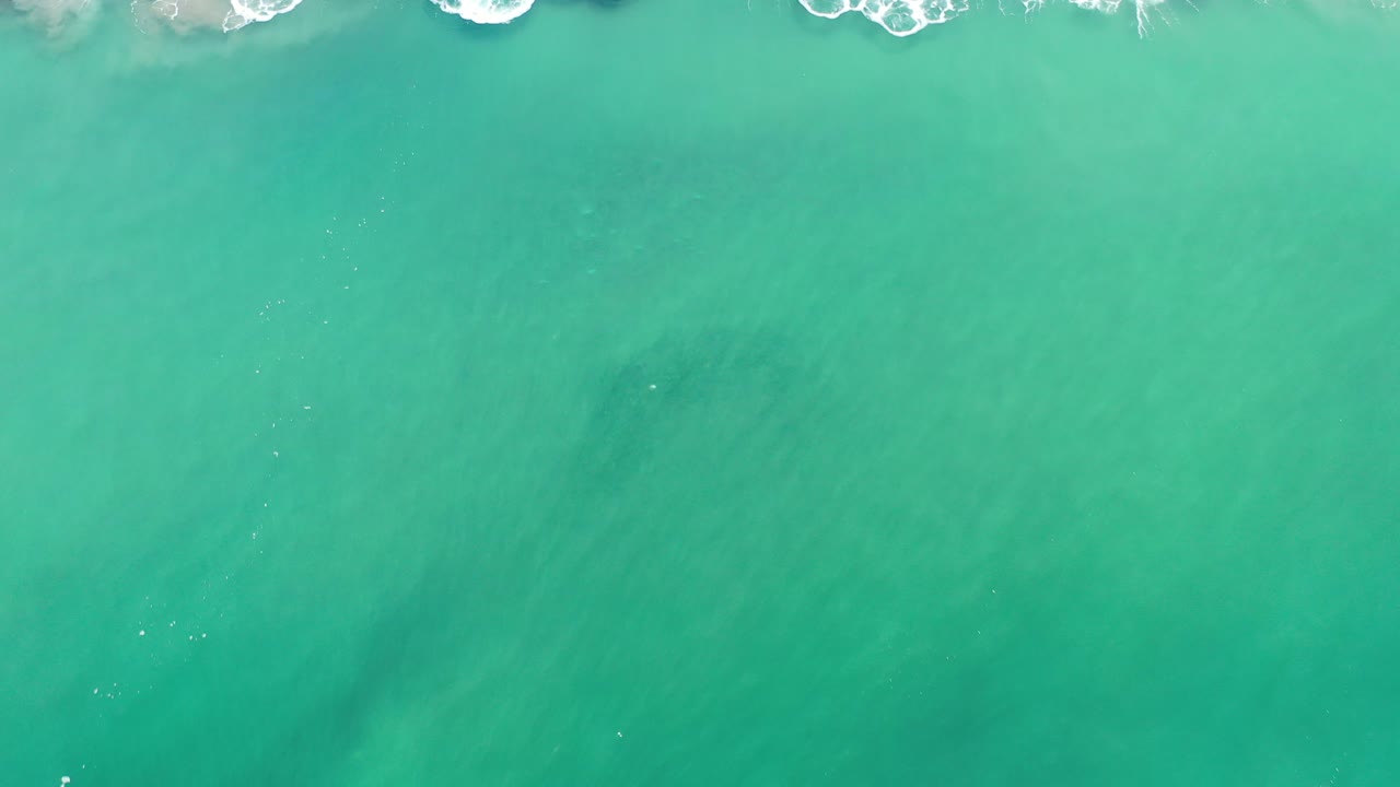 Overhead view of green ocean water in Los Cabos, Mexico, with white wave foam skimming the top edge and no visible people.