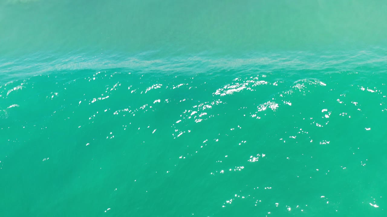 Turquoise ocean water in Los Cabos fills the frame, with a rippled surface band near the top, bright sun reflections, and no visible people.