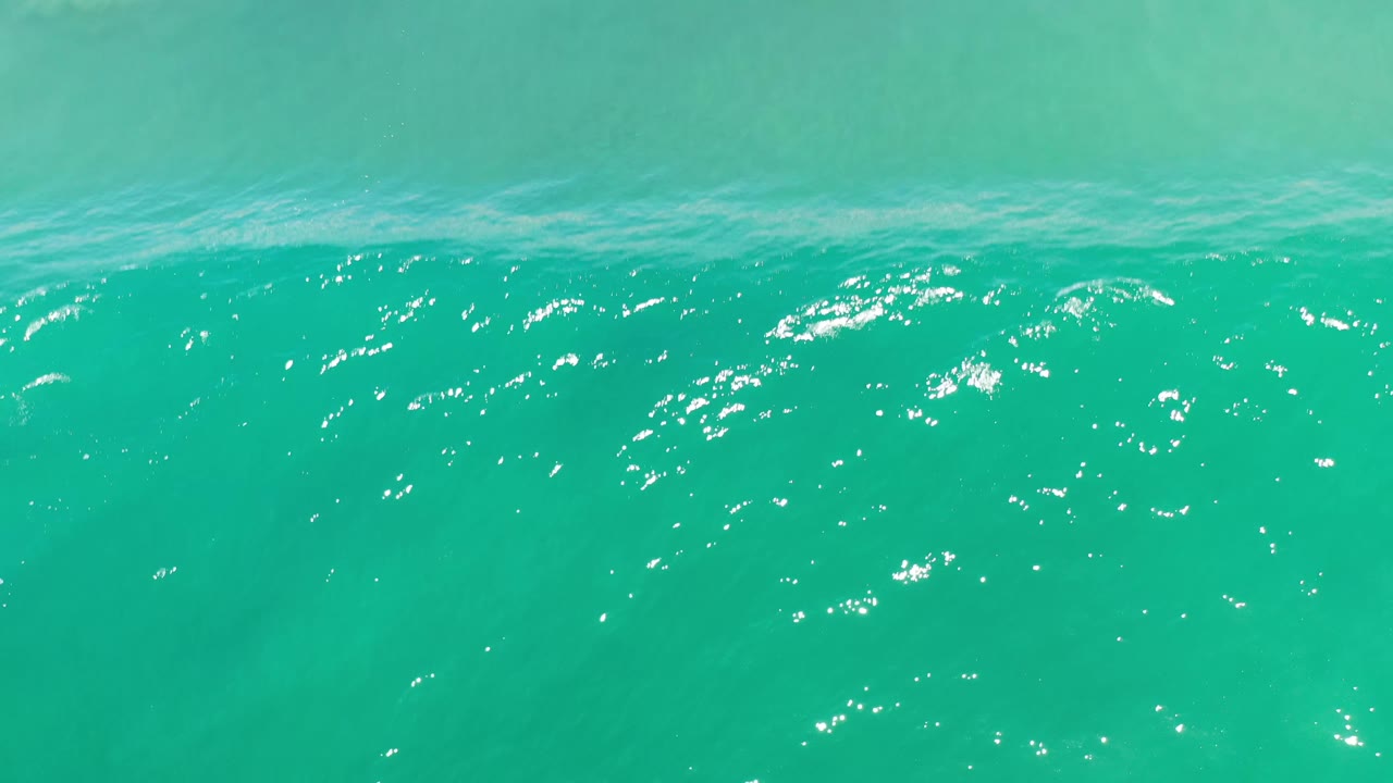 Bright teal Los Cabos ocean water shows a slightly raised ripple line across the upper frame, scattered white highlights, and no visible people.