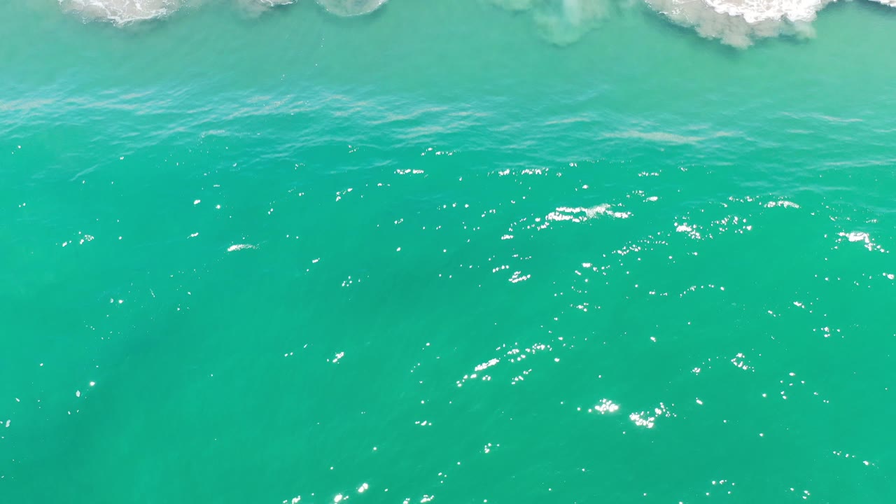 Open turquoise water with small white highlights and faint surf above.