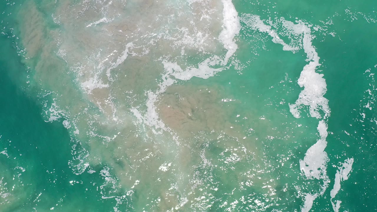 White foam patches crossing clear green beach water.