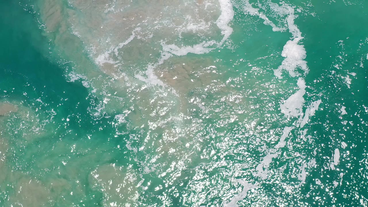 Top-down Los Cabos ocean frame with scattered white foam, dense sun glitter, darker green water, and no visible people.