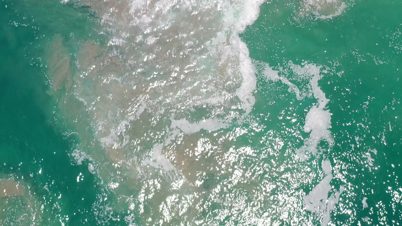 Overhead green seawater with white foam and sandy shallows.