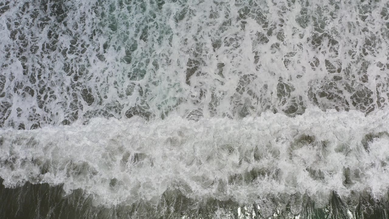 Top-down Los Cabos ocean frame filled with white surf foam over green-gray water, with no visible people.