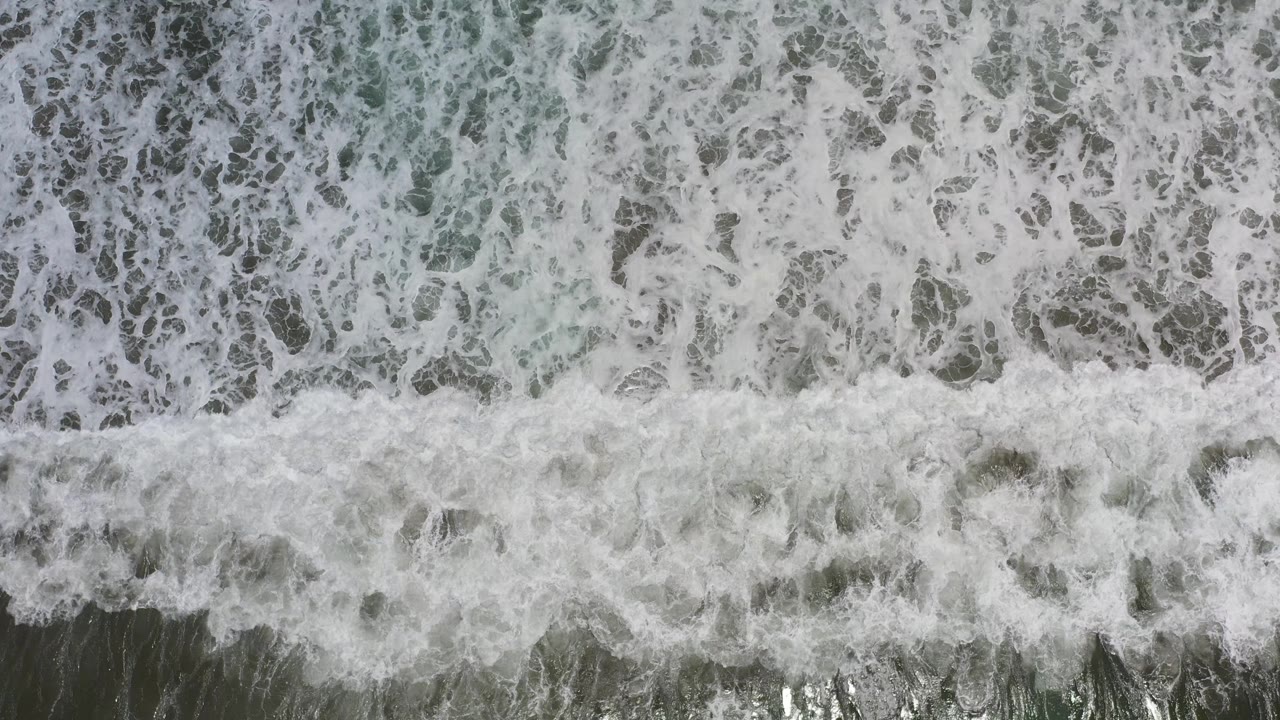 Overhead Los Cabos surf shows a stronger horizontal wave band crossing darker water, with no visible people.