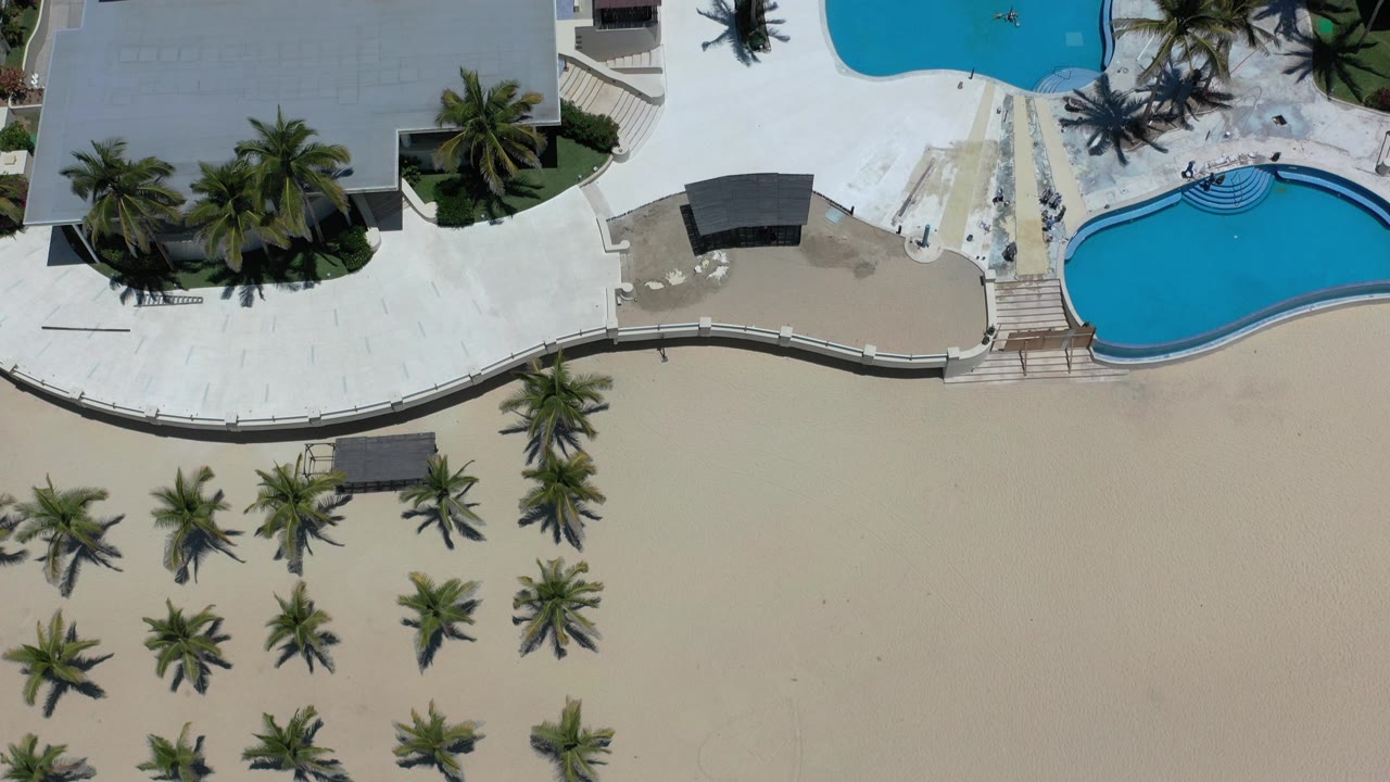 Overhead resort pools, palm trees, hotel roof, and sandy ground.