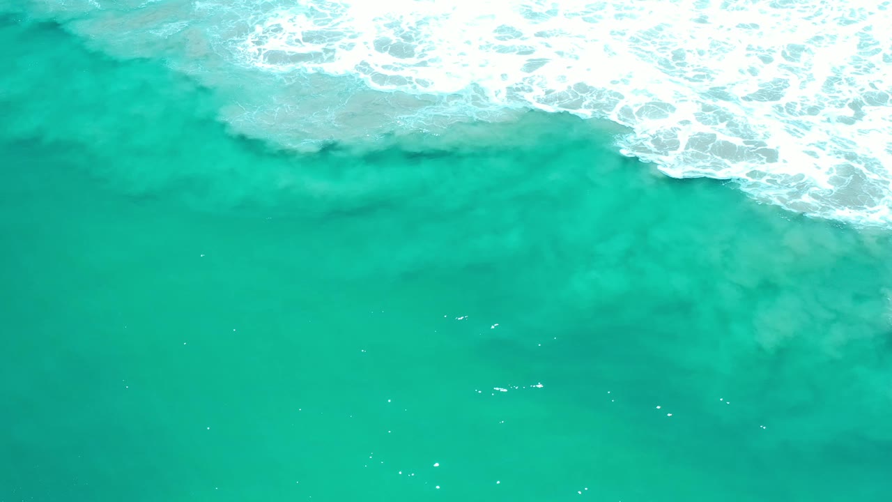 Green ocean water fills most of the frame in Los Cabos, Mexico, while white foam pushes across the upper edge with no visible people.