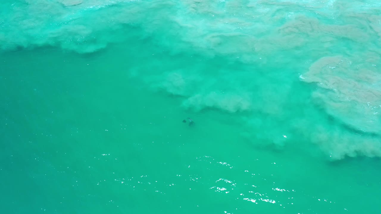 Blue-green Los Cabos ocean seen from above, with a broad pale wash drifting across the upper half and no visible people.