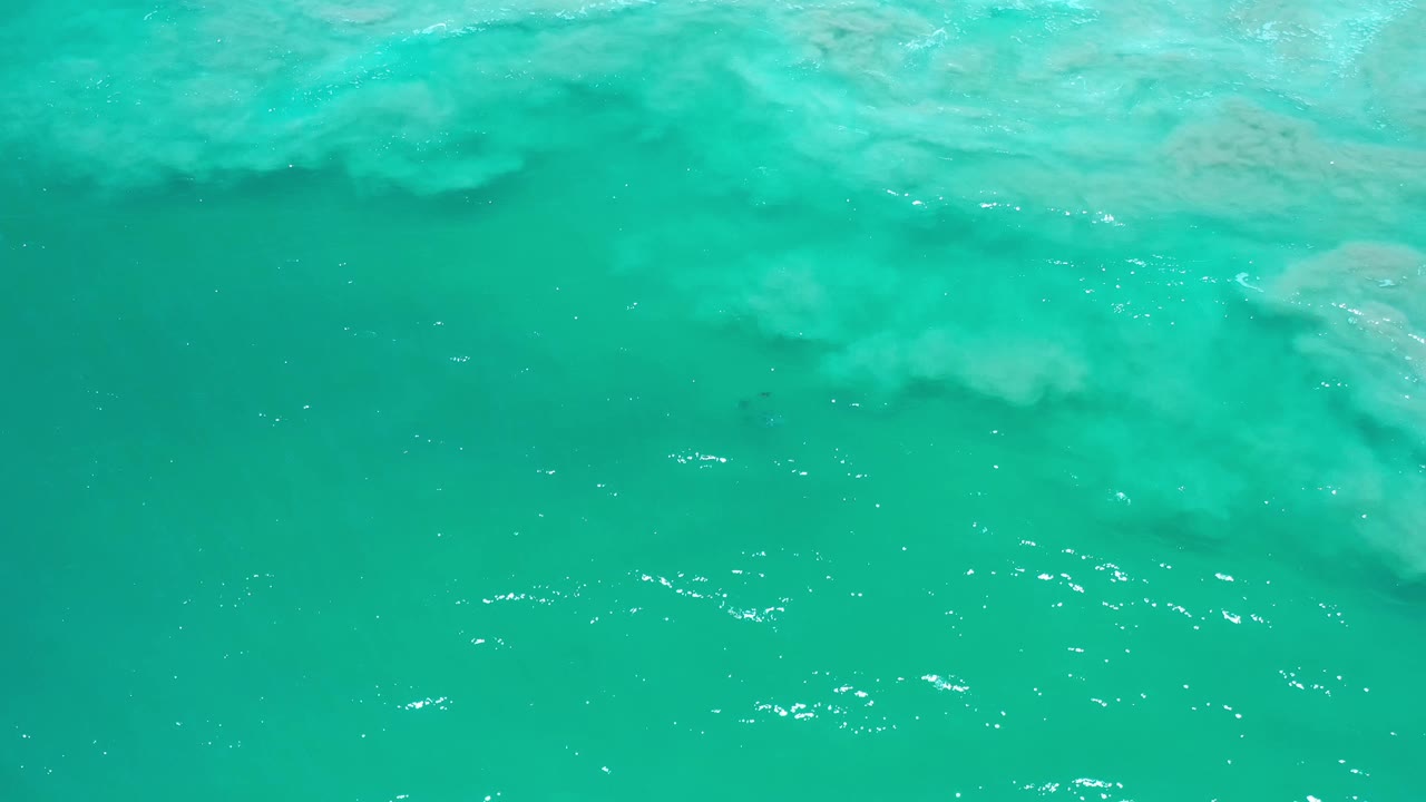 Turquoise sea surface in Los Cabos with small white highlights and a soft cloud of foam under the water, with no visible people.